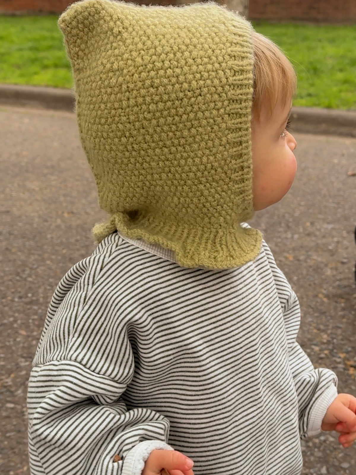 Baby wearing the Mio Balaclava, a pixie hood knitted in seed stitch in light green