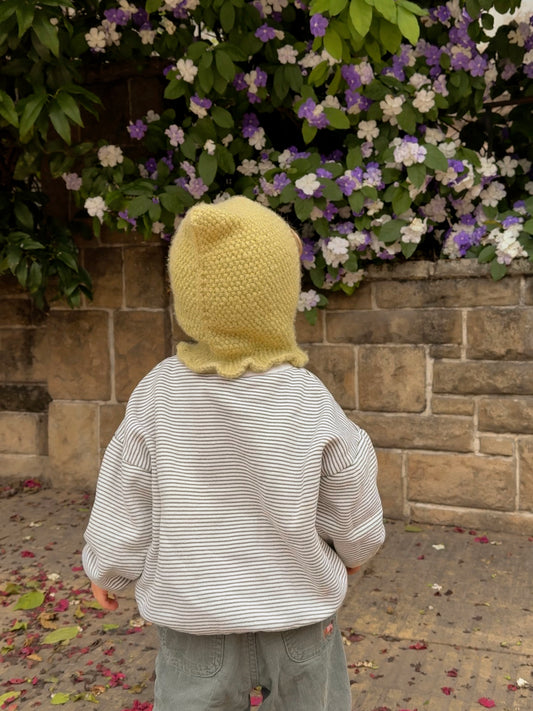 Baby wearing the Mio Balaclava, a pixie hood knitted in seed stitch in light green