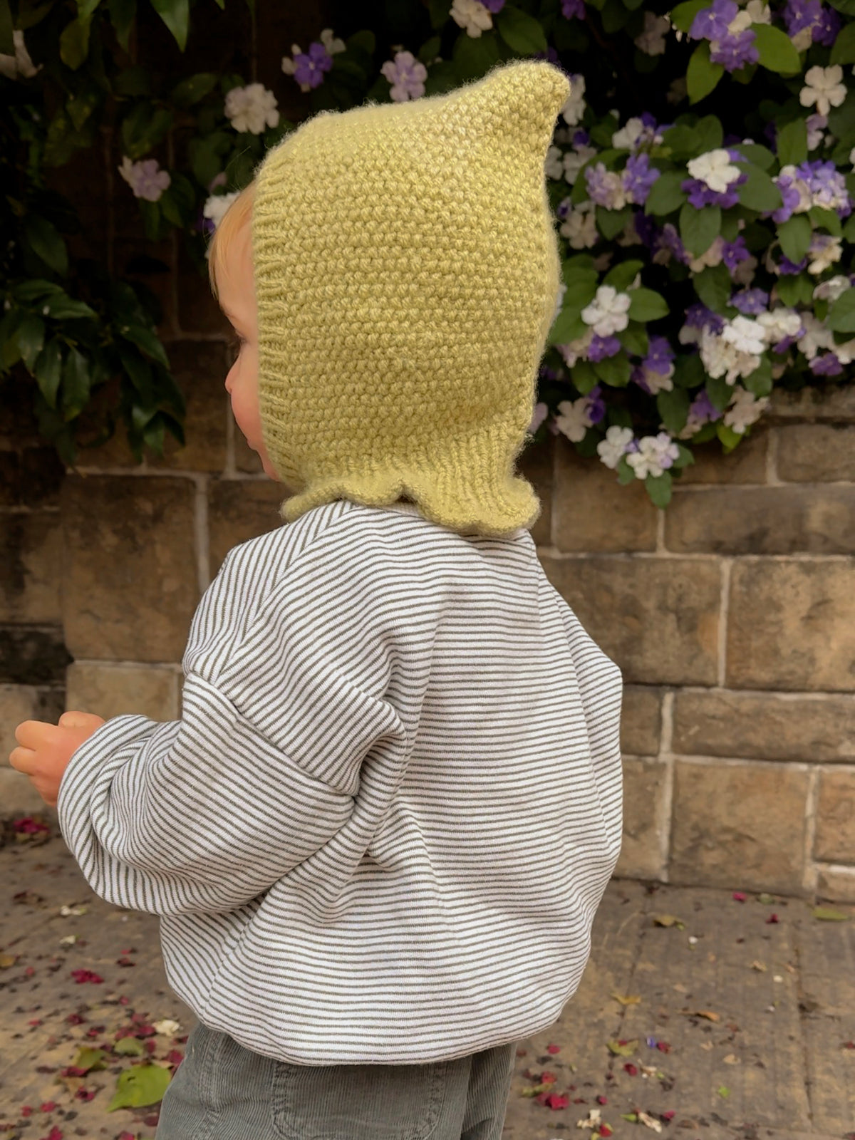 Baby wearing the Mio Balaclava, a pixie hood knitted in seed stitch in light green