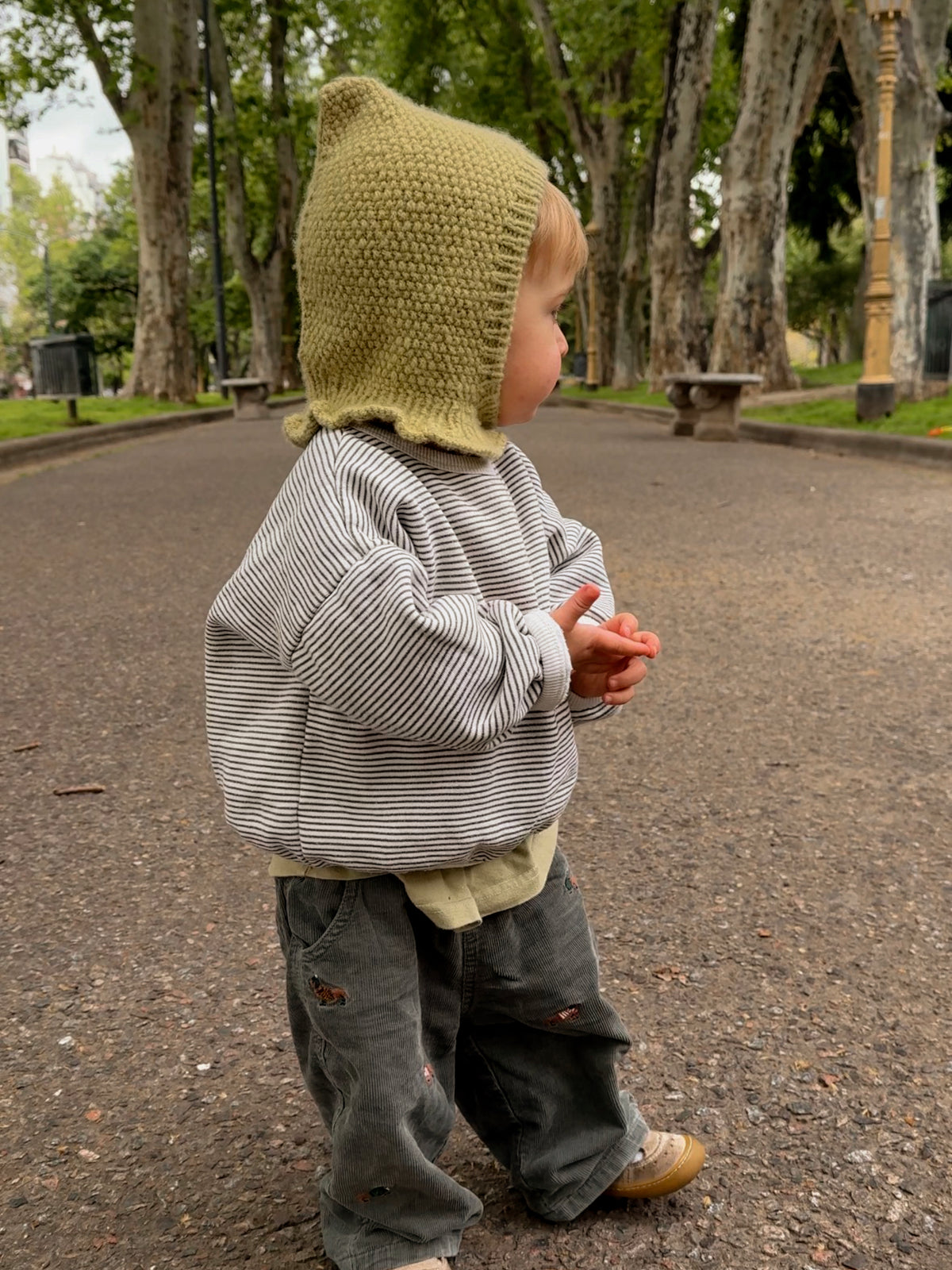 Baby wearing the Mio Balaclava, a pixie hood knitted in seed stitch in light green