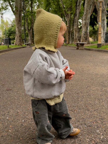 Baby wearing the Mio Balaclava, a pixie hood knitted in seed stitch in light green